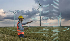 Engineer wearing hardhat and programming digital wind turbine through tablet PC in field - UUF31013