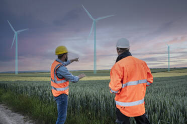 Engineer pointing at digital wind turbine design standing with colleague in field - UUF31016