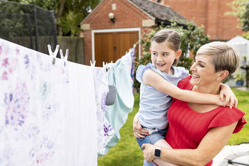 Glückliche Frau mit Tochter in der Nähe von Wäsche, die auf einer Wäscheleine im Hinterhof hängt - WPEF08129