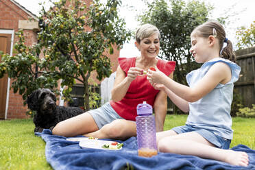 Lächelnde Frau verbringt ihre Freizeit mit ihrer Tochter auf einer Decke sitzend im Hinterhof - WPEF08149