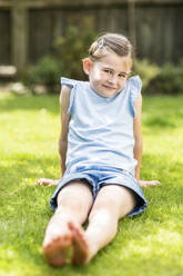 Smiling girl sitting on grass in garden - WPEF08154