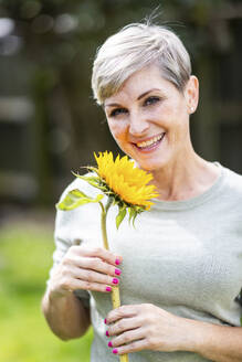 Glückliche Frau hält Sonnenblume im Garten - WPEF08162