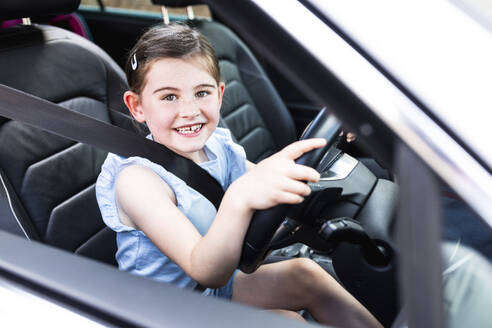 Happy girl holding steering wheel sitting in car - WPEF08175