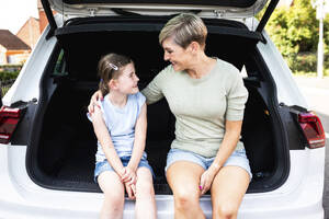 Lächelnde Frau mit einem Arm um ihre Tochter, die im Kofferraum eines Autos sitzt - WPEF08176