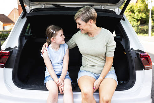 Smiling woman with arm around daughter sitting in car trunk - WPEF08176