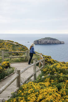 Frau lehnt sich an ein Geländer und schaut auf das Meer in Asturien, Spanien - MMPF01144