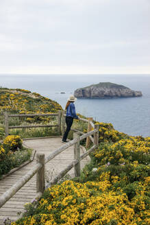 Woman leaning on railings and looking at sea in Asturias, Spain - MMPF01144