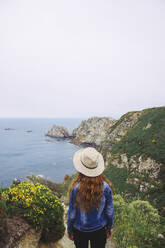 Rothaarige Frau mit Hut und Blick aufs Meer in Asturien, Spanien - MMPF01145