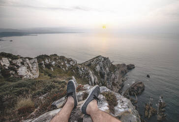 Junger Mann sitzt bei Sonnenuntergang auf einer Klippe am Meer - MMPF01152