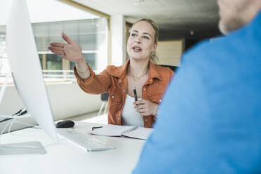 Businesswoman gesturing and having discussion with colleague in office - UUF31030