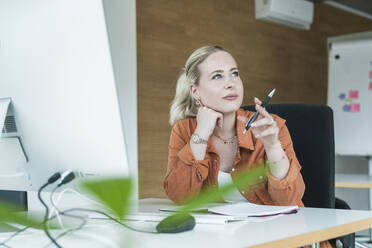 Nachdenkliche Geschäftsfrau hält Stift und sitzt im Büro - UUF31043