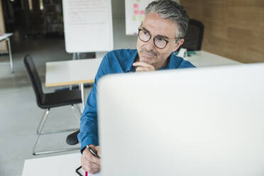 Nachdenklicher Geschäftsmann, der eine Brille trägt und am Schreibtisch im Büro sitzt - UUF31047