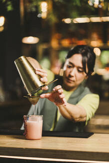 Bartender pouring cocktail drink in glass on bar counter - DAMF01279