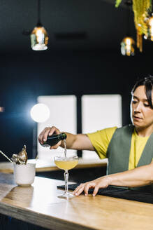 Bartender pouring drink in cocktail glass on bar counter - DAMF01282