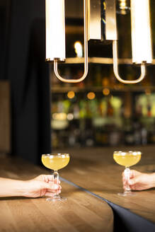 Hand of woman with cocktail drink on table near mirror in bar - DAMF01285