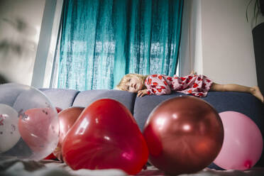 Mädchen auf dem Sofa liegend mit Luftballons zu Hause - ASHF00041