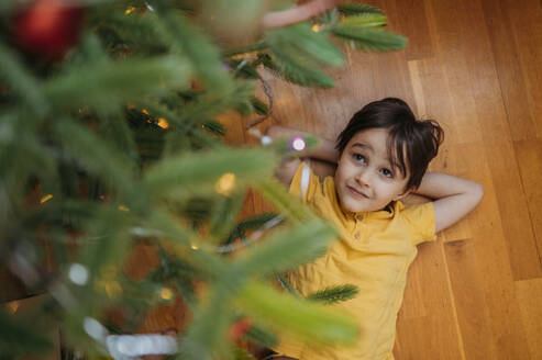 Junge auf dem Boden liegend unter dem Weihnachtsbaum zu Hause - ANAF02648
