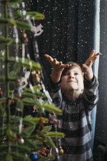 Verspielter Junge fängt falschen Schnee in der Nähe des Weihnachtsbaums zu Hause - ANAF02651