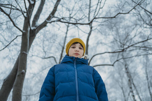 Junge mit Winterjacke in der Nähe von Bäumen im Wald - ANAF02654