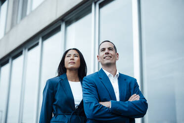 Happy businessman standing with arms crossed near colleague - JOSEF23059