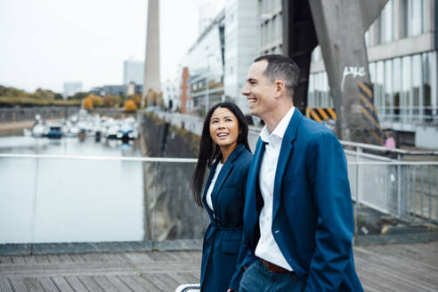 Smiling businessman and businesswoman walking near buildings - JOSEF23065