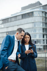 Businessman and businesswoman using smart phone in front of building - JOSEF23072