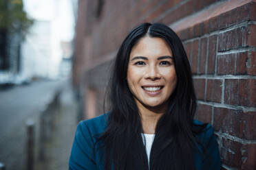 Happy businesswoman near brick wall - JOSEF23077