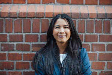 Smiling businesswoman in front of brick wall - JOSEF23079