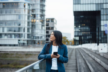 Thoughtful businesswoman standing near railing in front of buildings - JOSEF23084