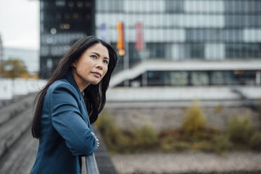 Contemplative businesswoman leaning on railing near building - JOSEF23097