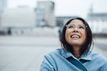 Happy businesswoman wearing eyeglasses at office park - JOSEF23100