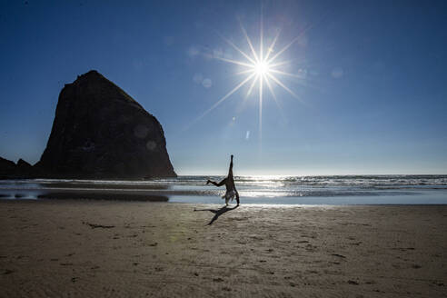 USA, Oregon, Silhouette einer Frau, die in der Nähe des Haystack Rock am Cannon Beach ein Rad schlägt - TETF02377