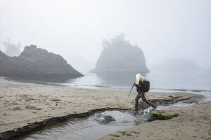 USA, Oregon, Brookings, Ältere Frau wandert mit Nordic-Walking-Stöcken am Strand - TETF02392