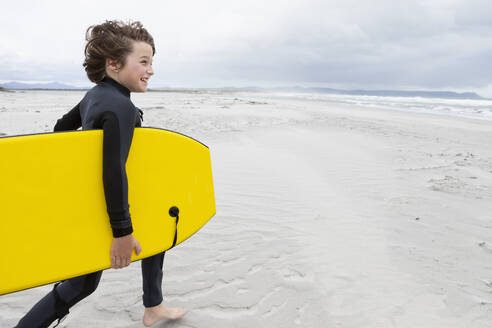 Junge (10-11) läuft am Strand und trägt ein Bodyboard - TETF02421