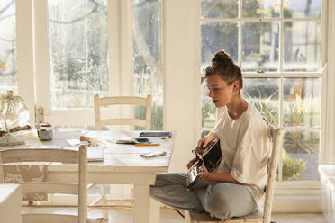 Teenage girl (16-17) playing guitar in dining room - TETF02436