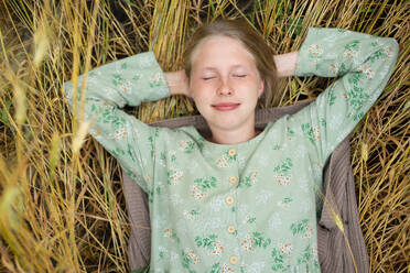 Junge Frau liegt mit geschlossenen Augen auf einem Feld - TETF02456