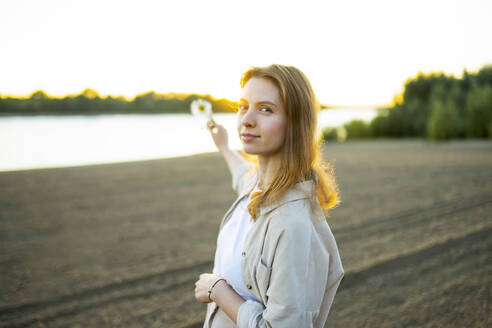 Portrait of woman holding flower on beach at sunset - TETF02459