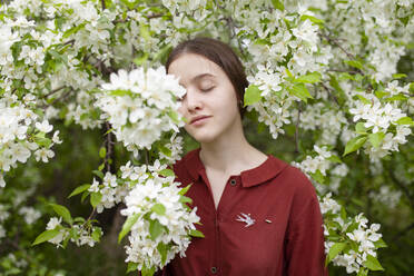 Junge Frau steht mit geschlossenen Augen an einem blühenden Baum - TETF02466