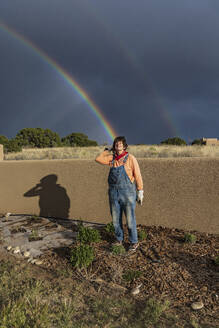 USA, New Mexico, Santa Fe, Porträt einer Frau im Garten mit doppeltem Regenbogen im Hintergrund - TETF02472