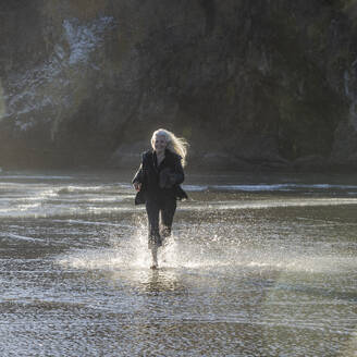 USA, Oregon, Newport, Frau läuft am Sandstrand und plantscht im Wasser - TETF02481