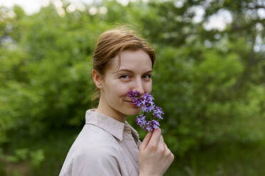 Portrait of smiling woman smelling lilac flower - TETF02522