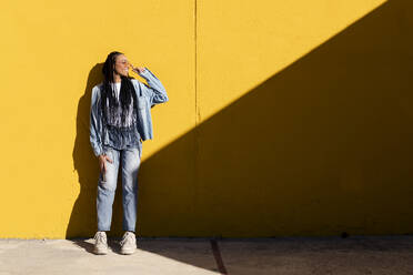 Smiling woman leaning on yellow wall - LMCF00771