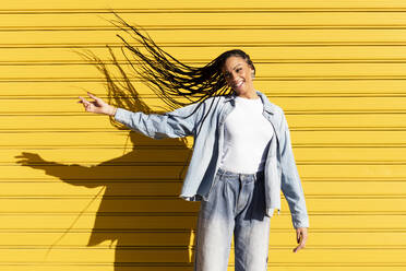 Happy young woman tossing hair in front of corrugated shutter - LMCF00774