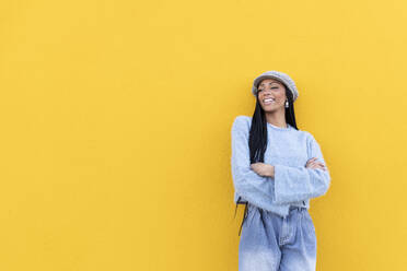 Woman with arms crossed standing in front of yellow wall - LMCF00787