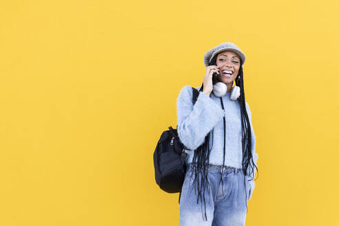 Fröhliche Frau, die vor einer gelben Wand mit ihrem Smartphone telefoniert - LMCF00789