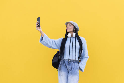 Junge Frau, die ein Selfie mit ihrem Smartphone vor einer gelben Wand macht - LMCF00790