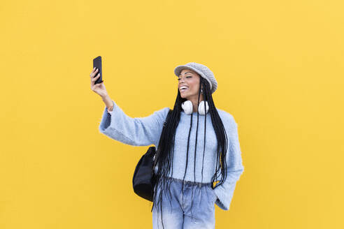 Fröhliche Frau, die ein Selfie vor einer gelben Wand macht - LMCF00791