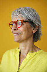 Smiling woman wearing eyeglasses against yellow background - EBSF04354