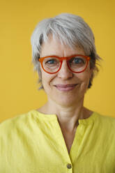 Smiling mature woman wearing eyeglasses against yellow background - EBSF04355