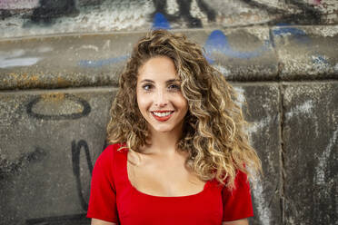 Smiling woman with curly hair in front of wall - BFRF02444